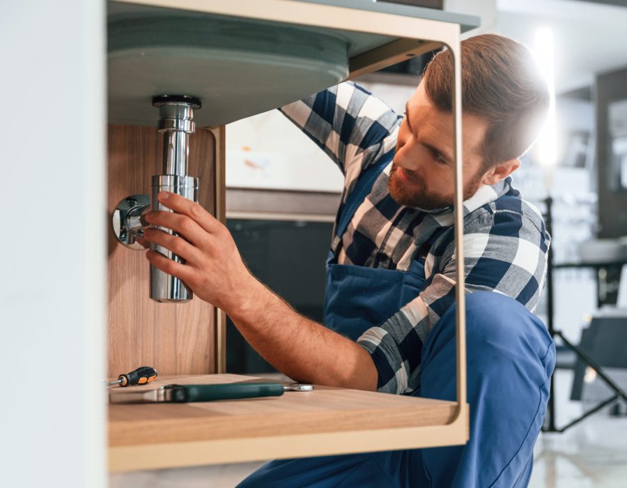 Busy by repairing siphon. Plumber in blue uniform is at work in the bathroom Busy by repairing siphon. Plumber in blue uniform is at work in the bathroom.